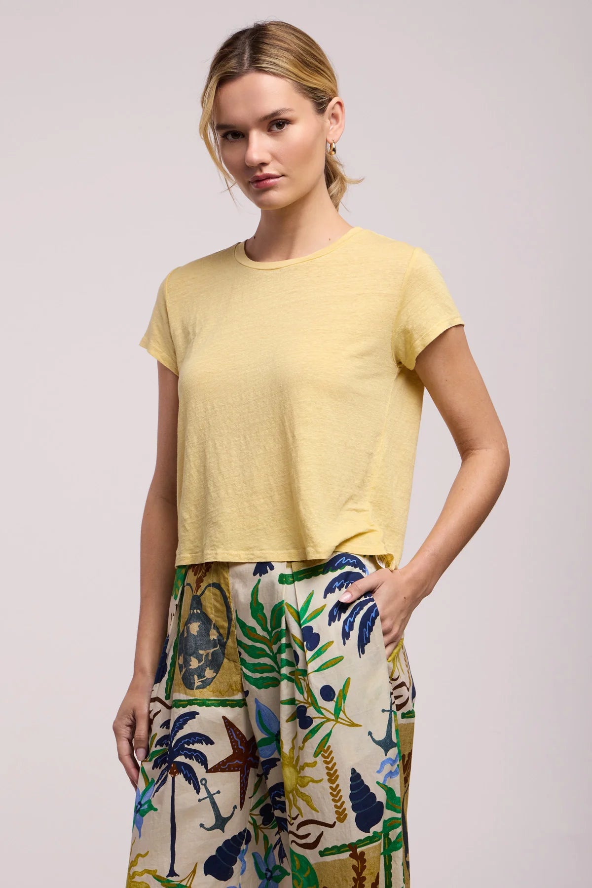 Woman wearing a yellow top and colorful patterned pants on a plain background
