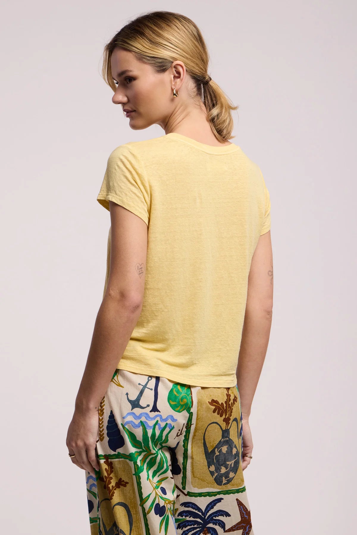 Woman wearing a yellow t-shirt and colorful pants on a light pink background