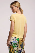Woman wearing a yellow t-shirt and colorful pants on a light pink background