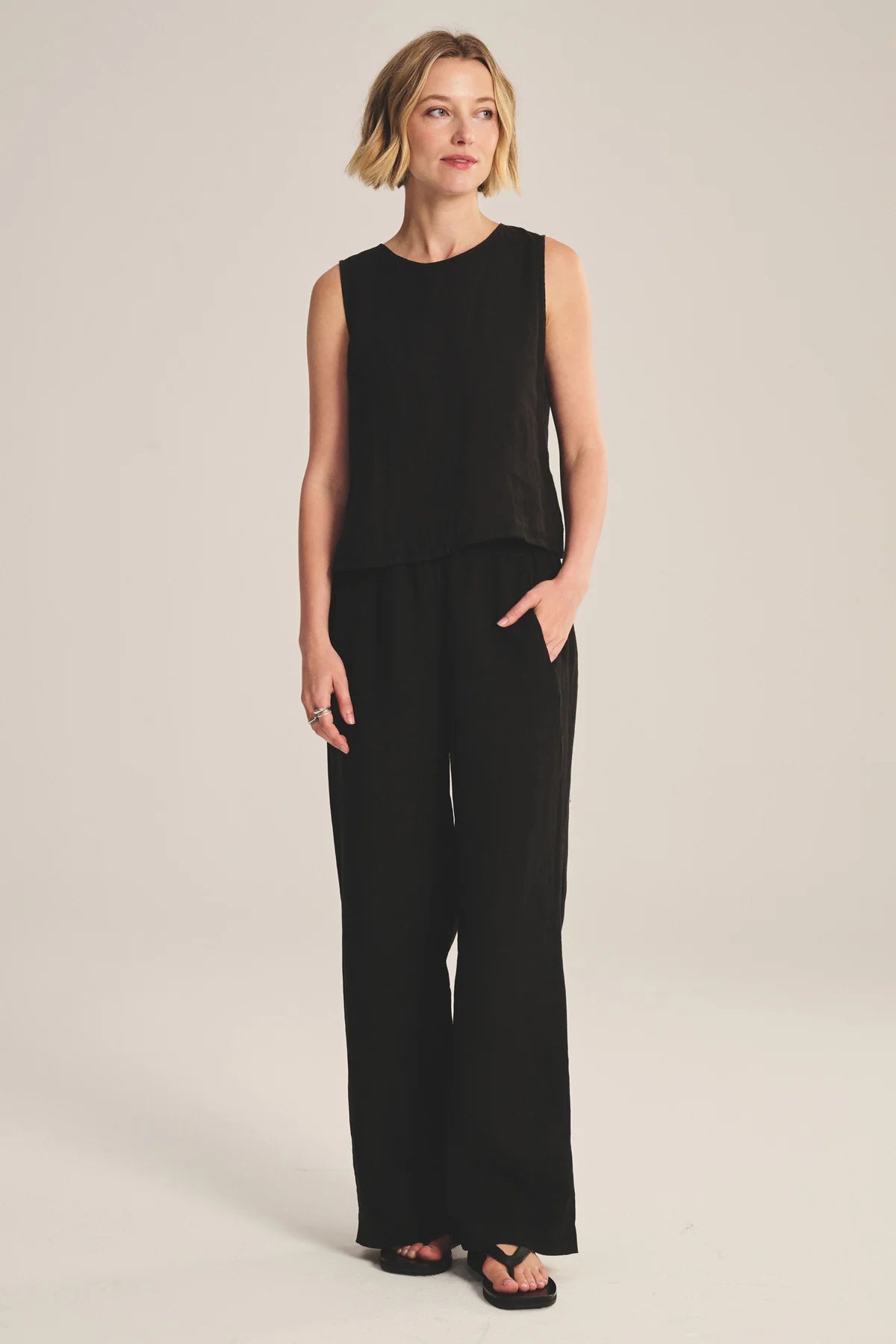 Woman wearing a black sleeveless top and wide-leg pants on a beige background