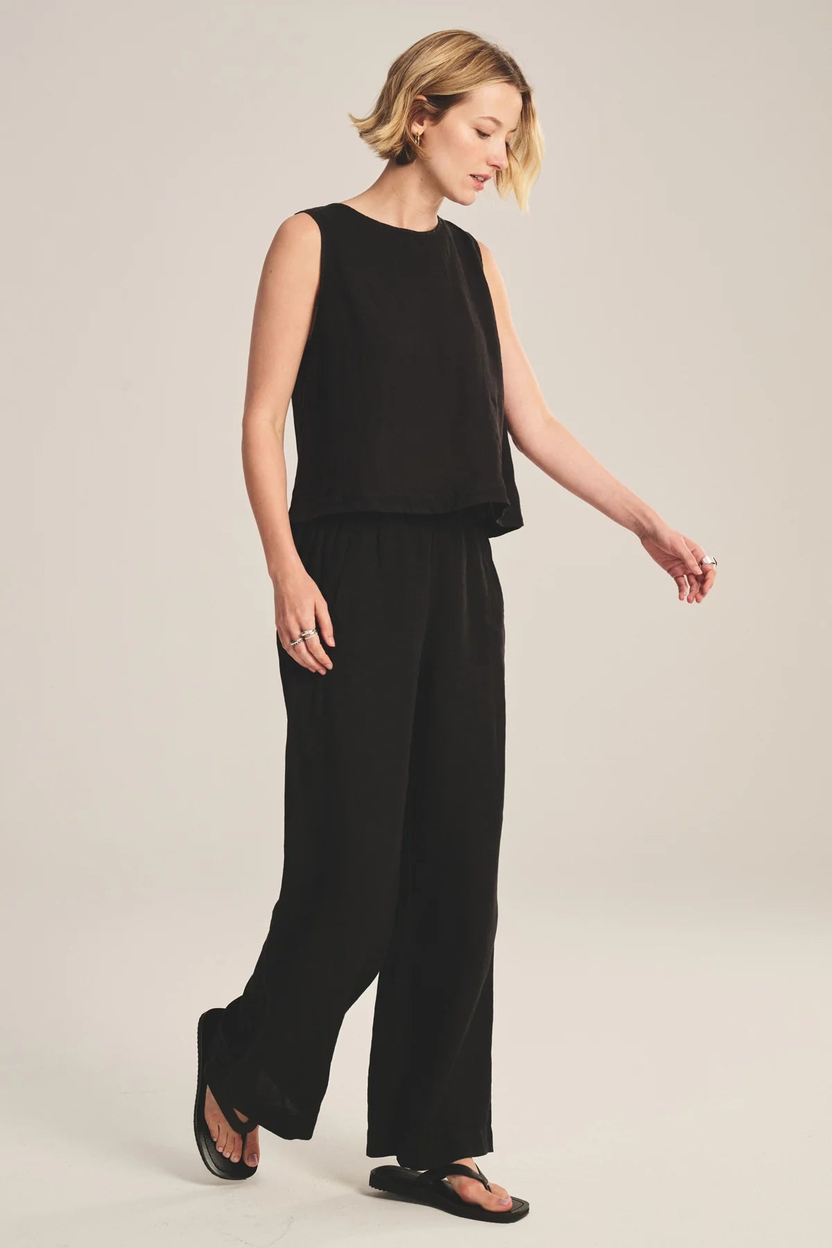 Woman wearing a black sleeveless top and wide-leg pants on a beige background
