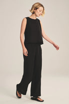Woman wearing a black sleeveless top and wide-leg pants on a beige background