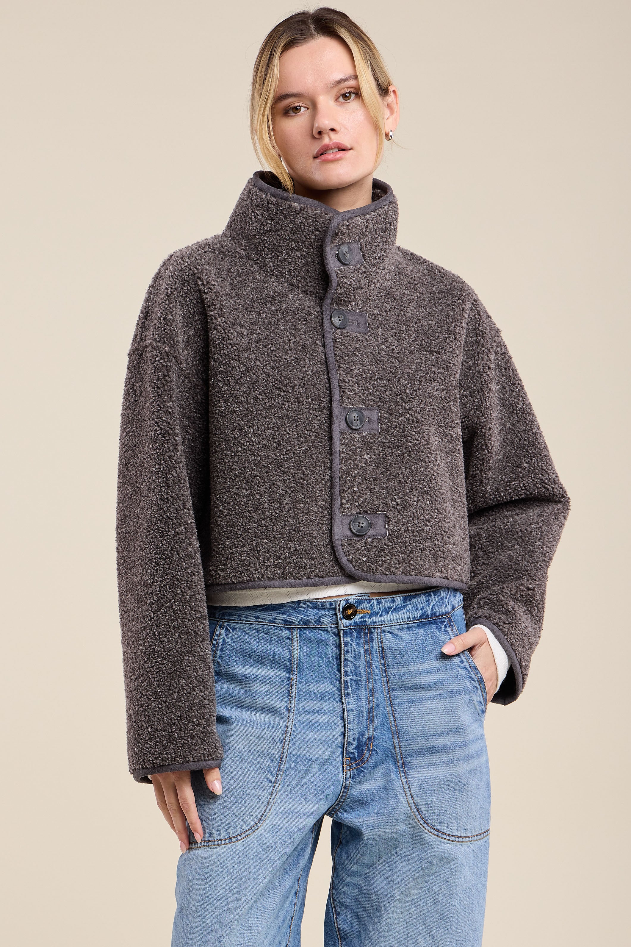 Woman wearing a brown textured jacket and blue jeans on a beige background