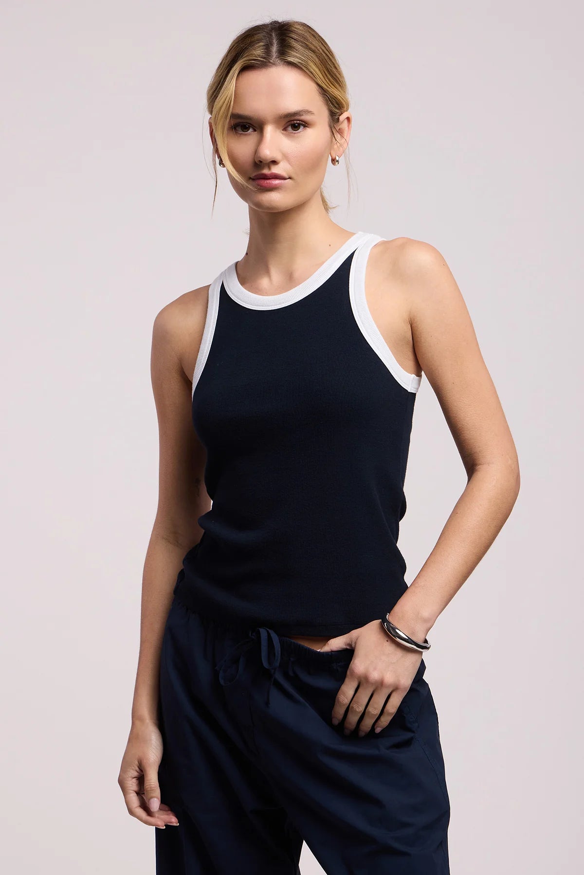 Woman wearing a navy tank top and pants on a light pink background