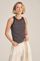 Woman wearing a black and white striped sleeveless top with white pants on a plain background