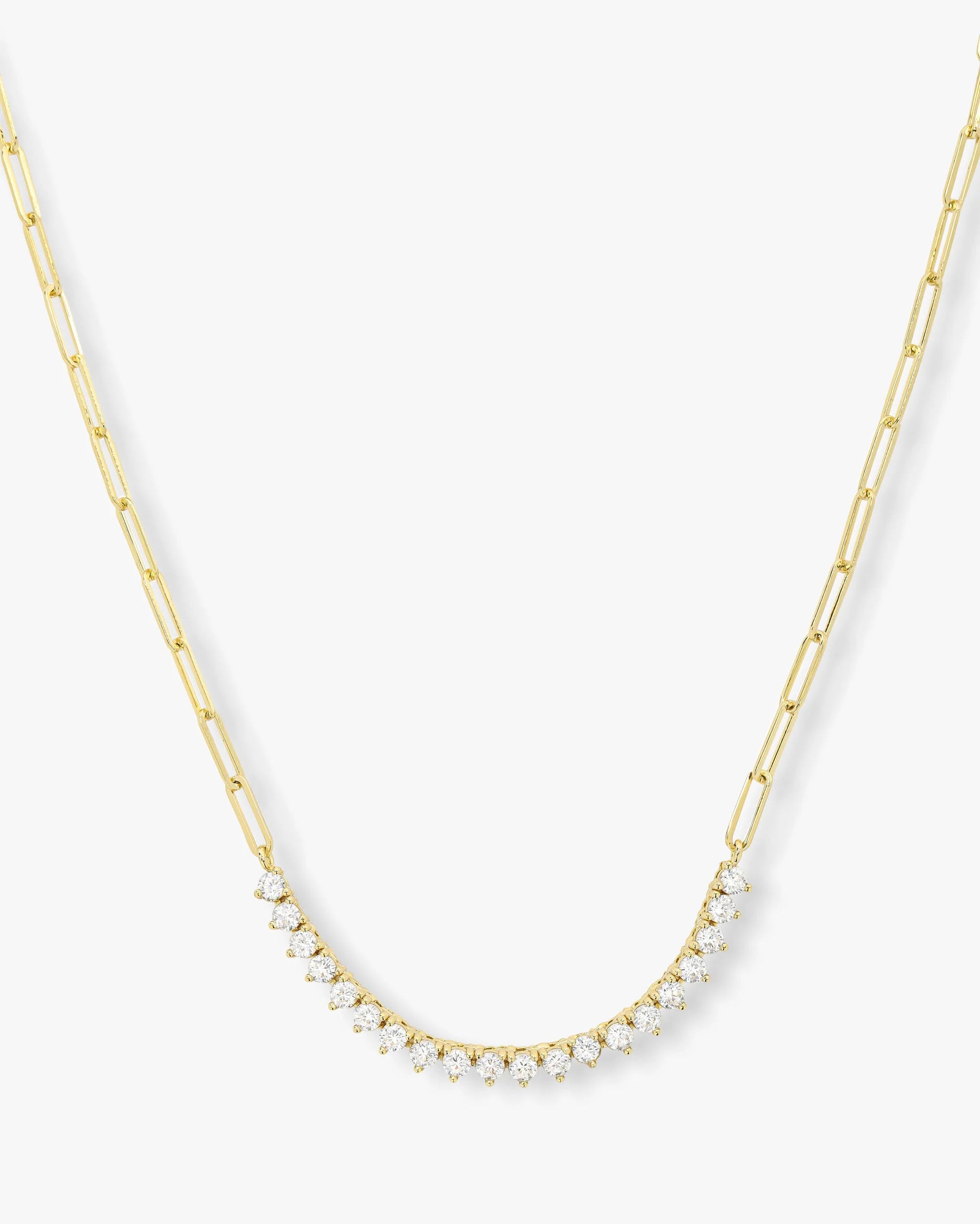 A gold paperclip chain necklace featuring a curved row of small clear stones at the center, displayed against a clean white background.