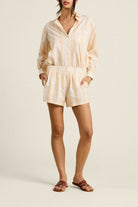 Woman wearing a beige and white striped romper on a plain background