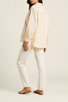 Person wearing a light-colored shirt and white pants on a plain background
