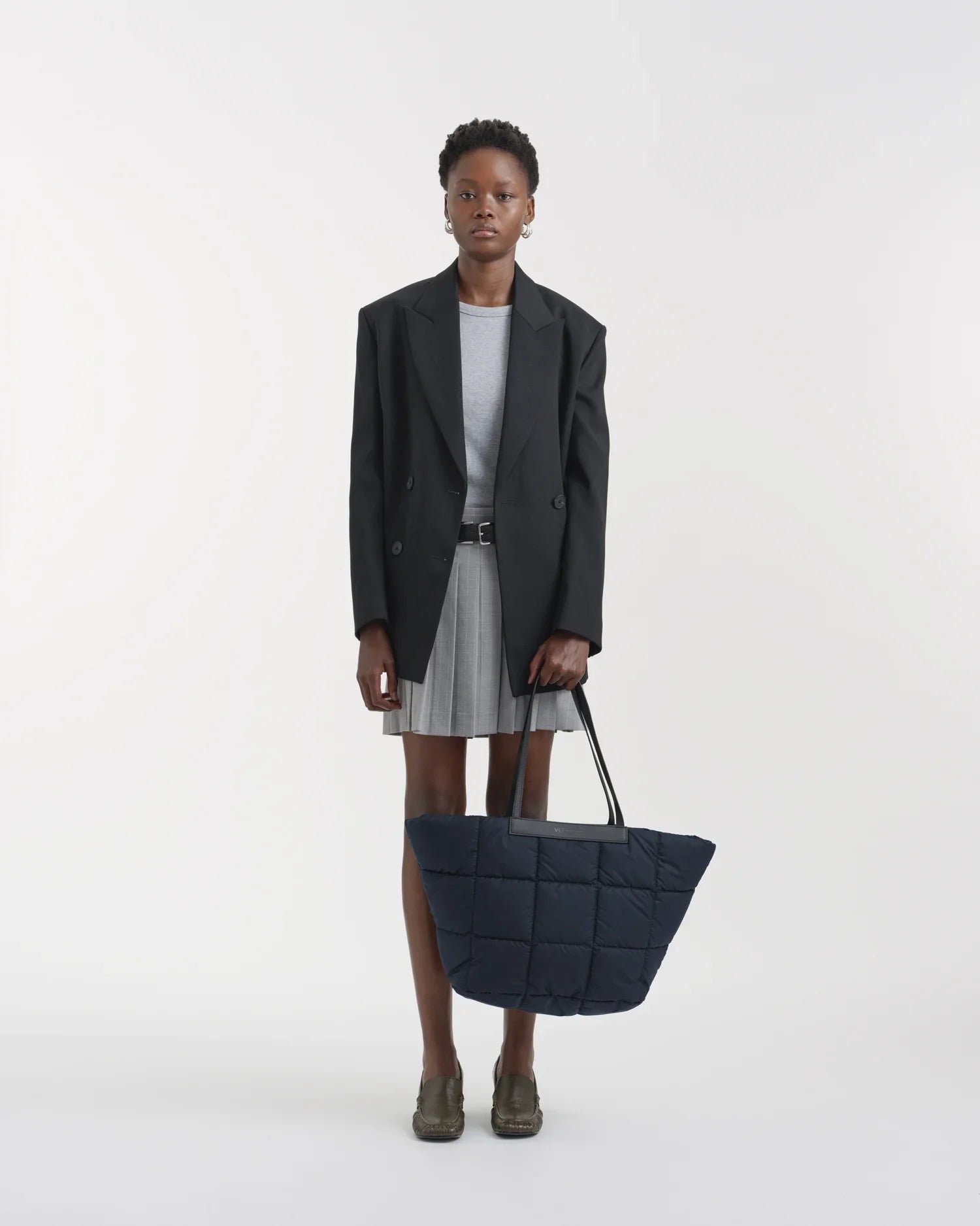 Person wearing a black blazer and holding a navy blue quilted bag on a white background