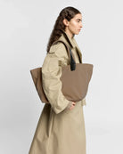 Woman holding a large beige tote bag against a white background