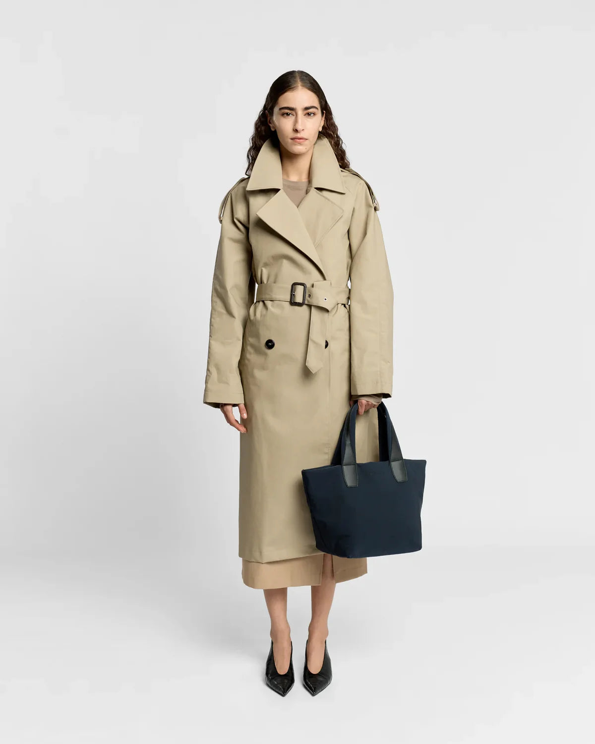 Woman wearing a beige trench coat holding a black handbag on a white background