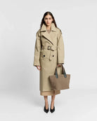 Woman wearing a beige trench coat holding a matching tote bag on a white background
