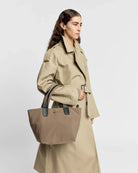 Woman holding a beige tote bag against a plain background