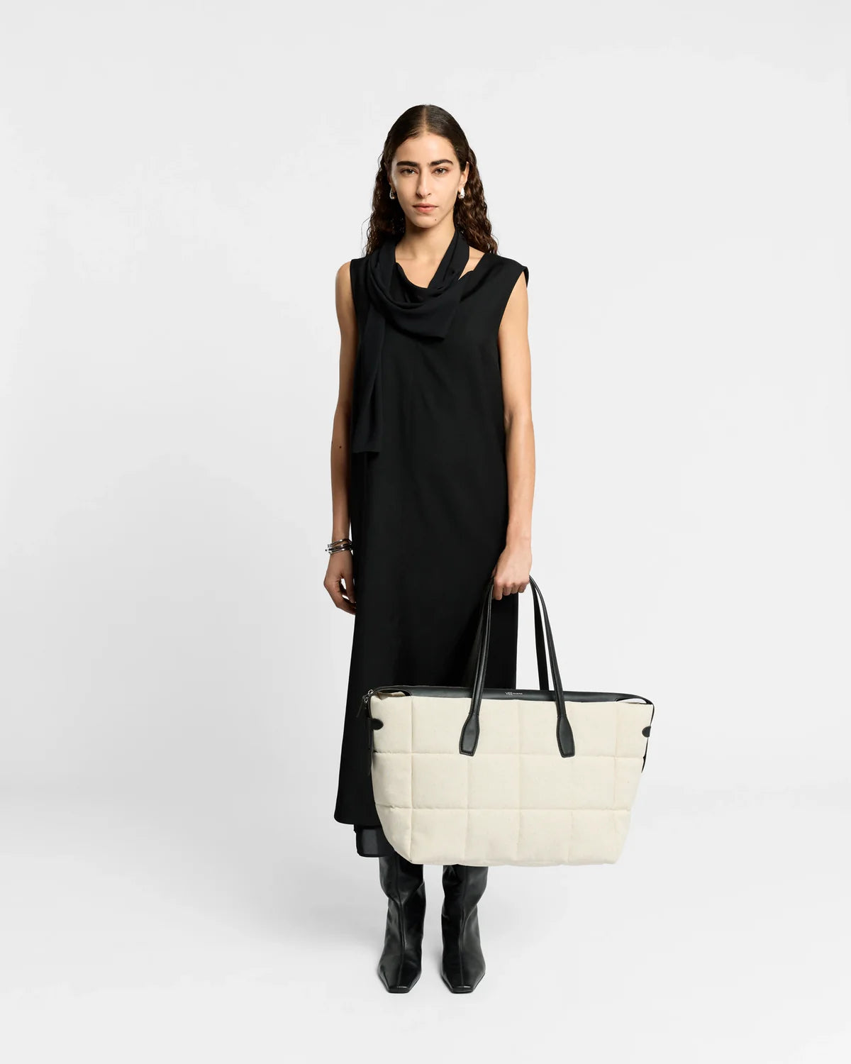 Woman holding a white quilted handbag against a plain background