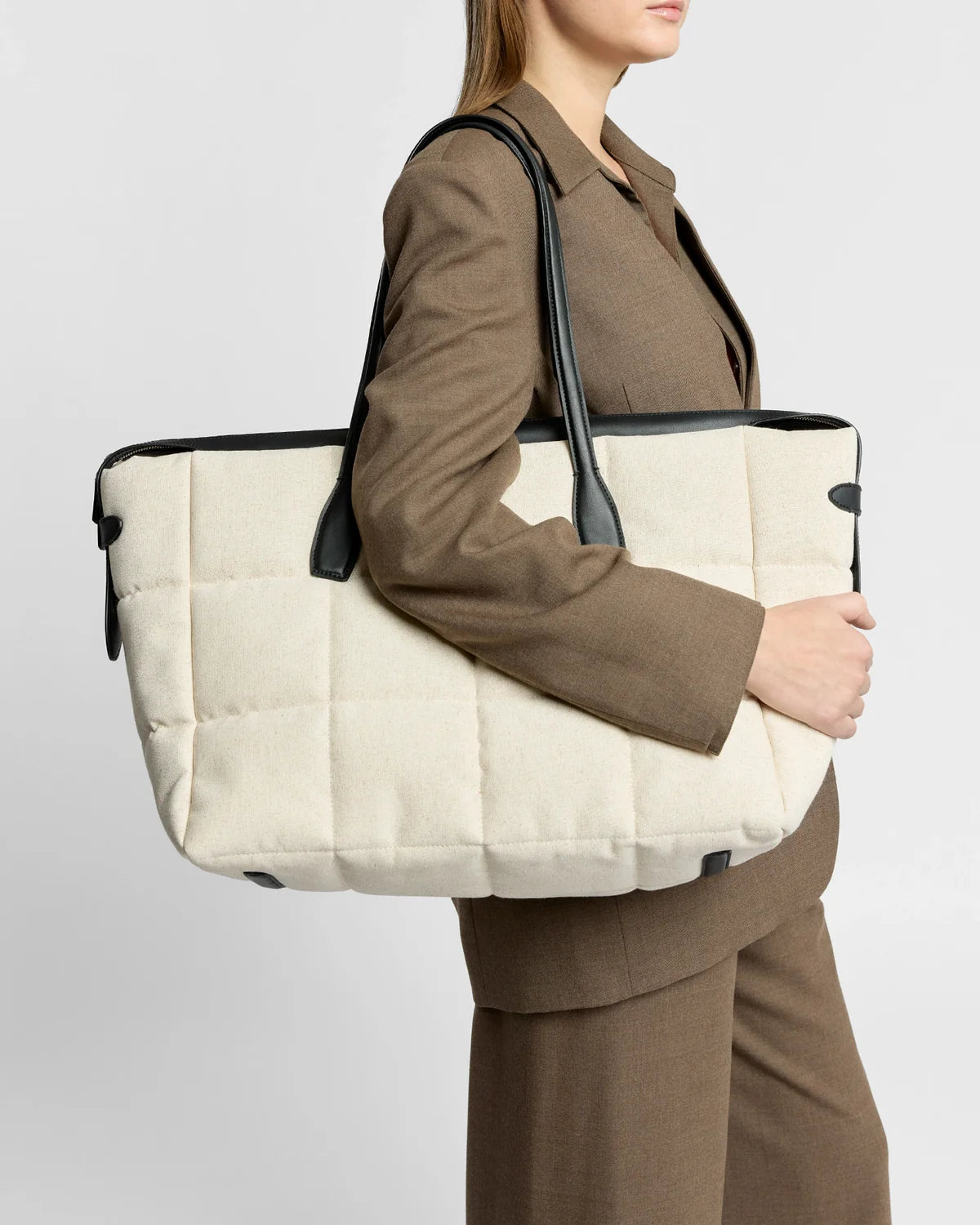 Person holding a large beige tote bag with black handles against a plain background