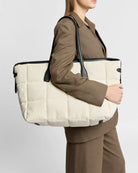 Person holding a large beige tote bag with black handles against a plain background