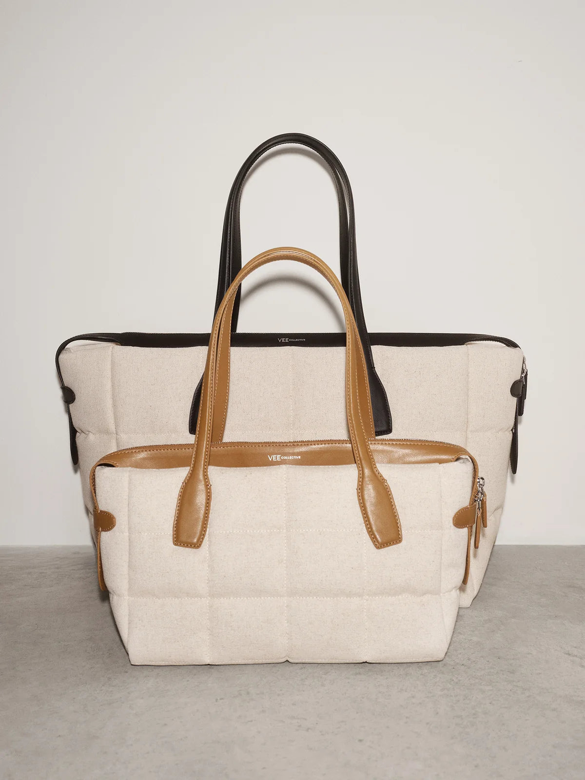 Two handbags, one beige with brown handles and the other black with brown handles, on a light gray background.