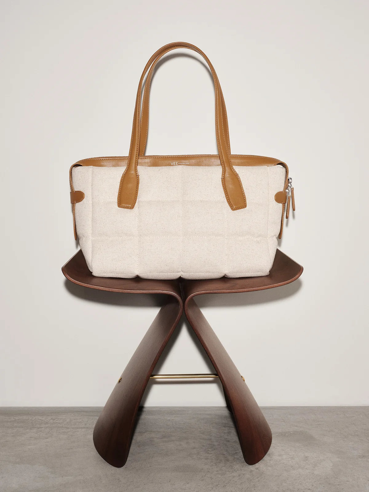 White quilted handbag with brown leather handles and trim on a wooden stand against a light background