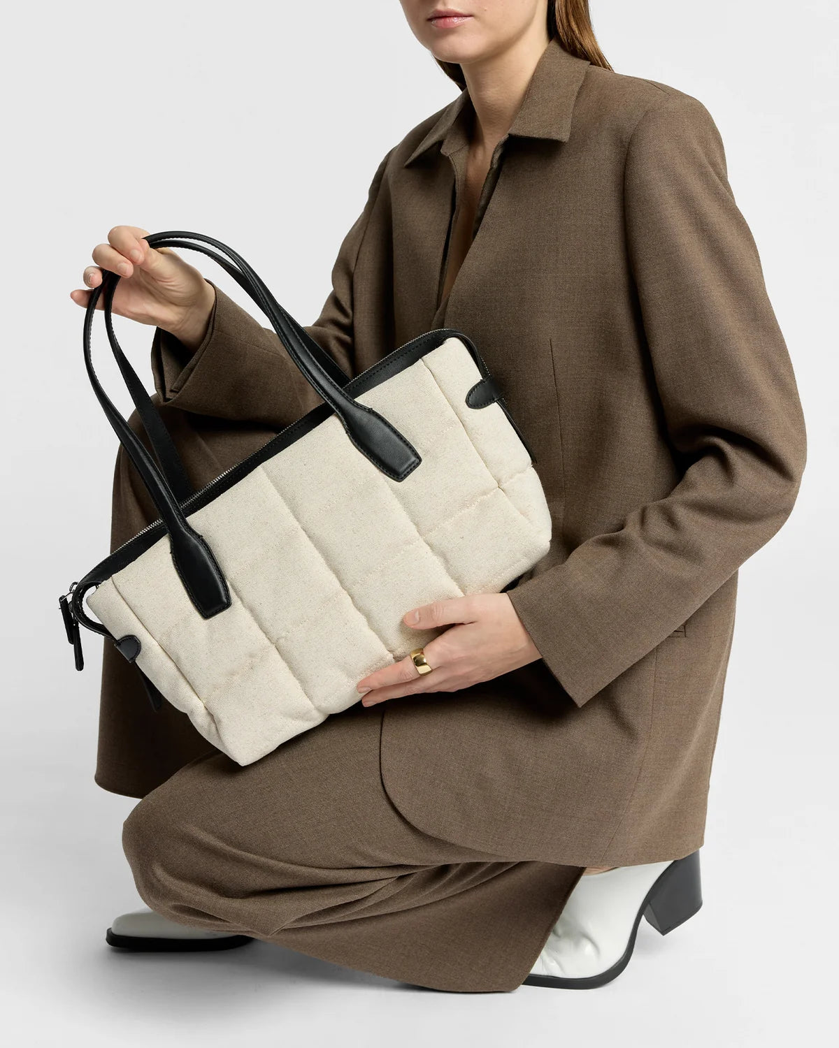 Person holding a beige quilted handbag with black handles against a white background