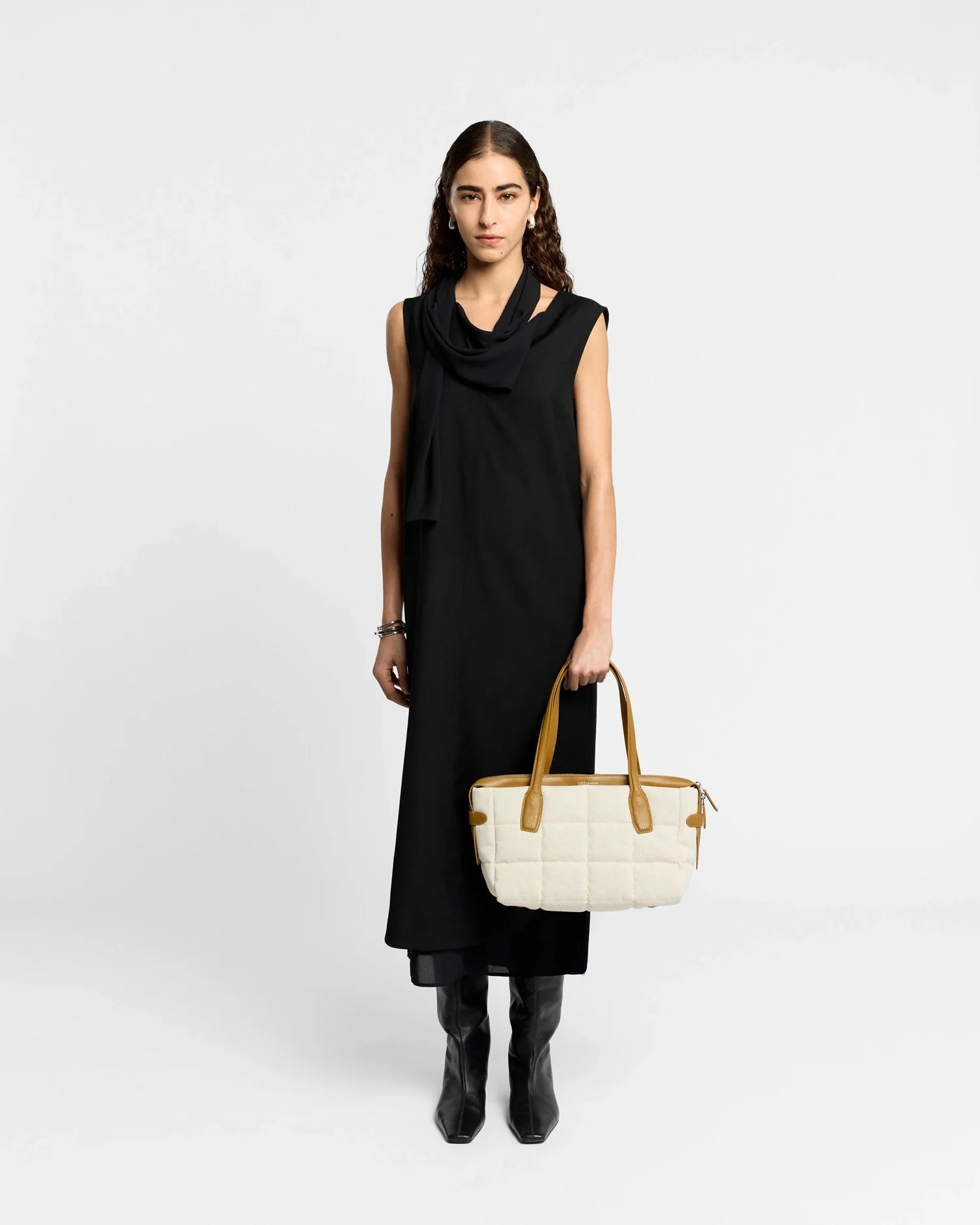 Woman in a black dress holding a white handbag against a white background