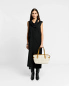 Woman in a black dress holding a white handbag against a white background