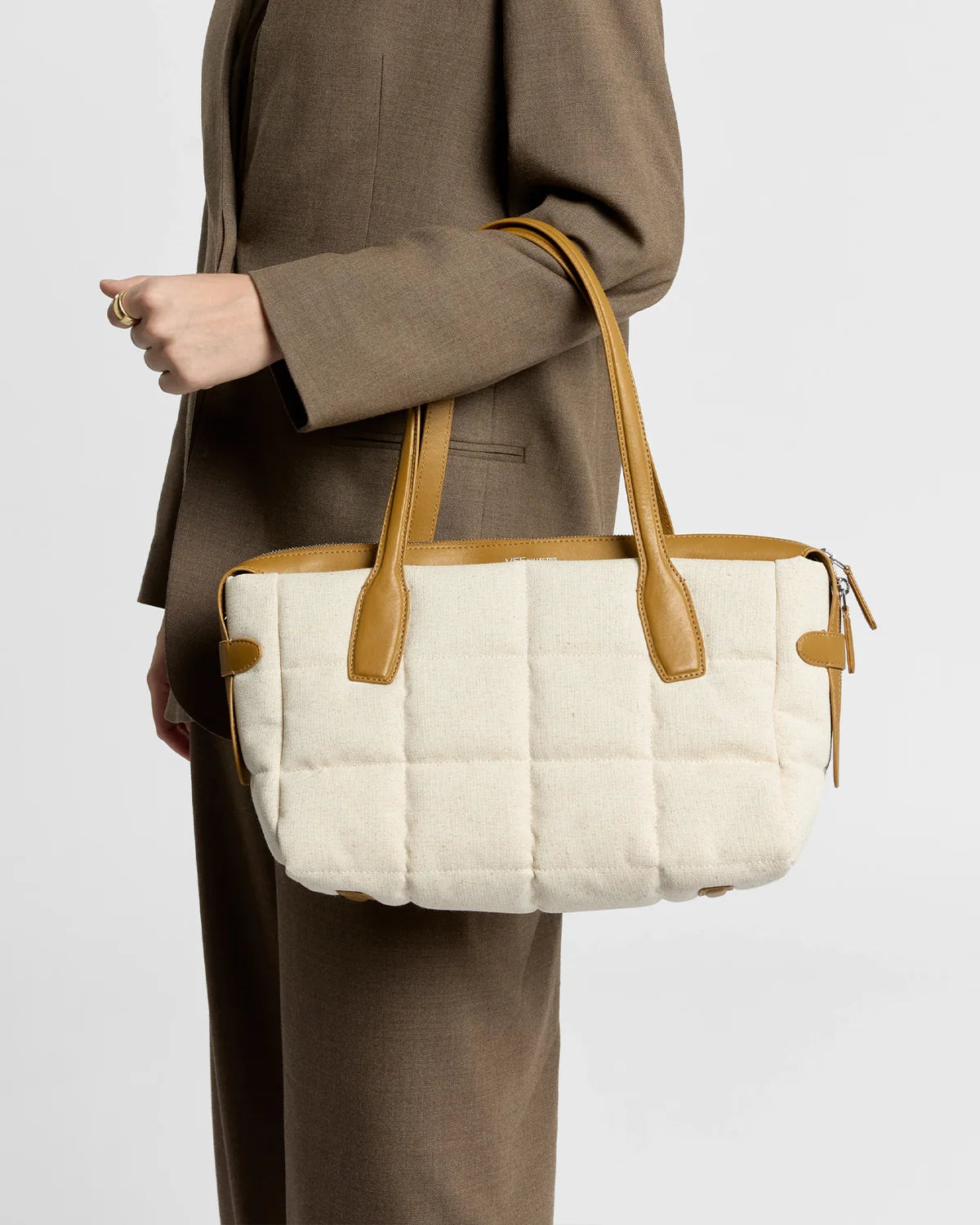 Person holding a beige quilted handbag with brown straps against a neutral background
