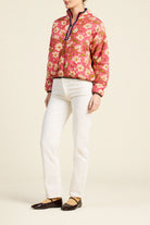 A model wearing a pink floral quarter-zip pullover sweater, white pants, and brown Mary Jane flats, standing against a solid beige background.