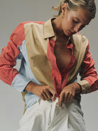 Woman wearing a red and white striped shirt with a beige vest over a blue shirt, against a neutral background.