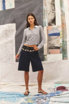 Woman wearing a light gray shirt and black shorts standing in front of a textured wall.