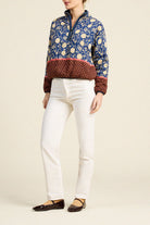 A model wearing a blue and beige floral quarter-zip pullover with a burgundy patterned hem, paired with white pants and dark brown flats, against a solid light beige background.