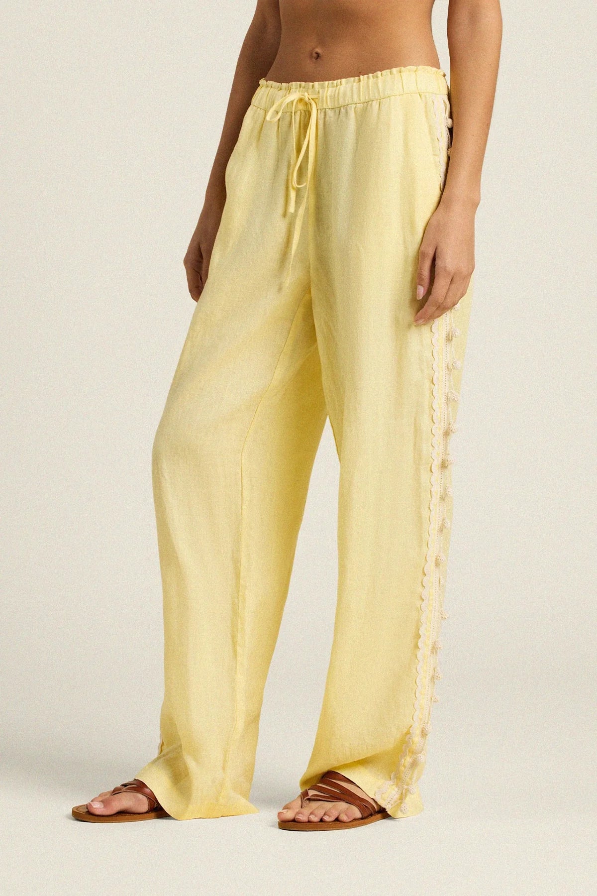 Person wearing light yellow pants with a drawstring on a plain background