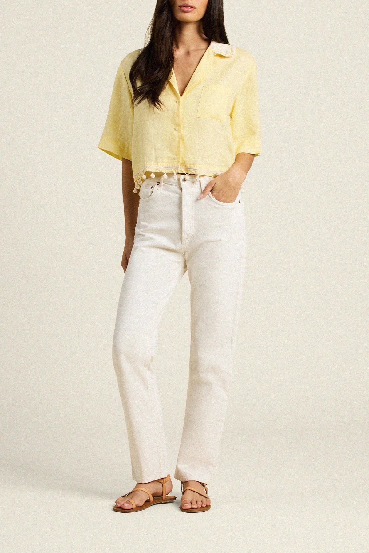 Woman wearing a yellow blouse and white pants on a plain background