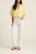 Woman wearing a yellow blouse and white pants on a plain background