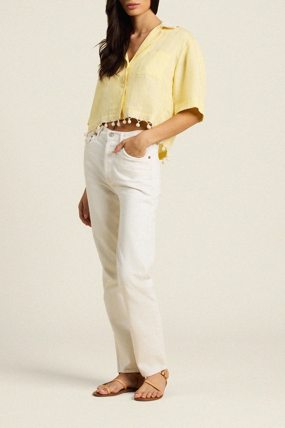 Woman wearing a yellow blouse and white pants on a plain background