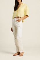 Woman wearing a yellow blouse and white pants on a plain background