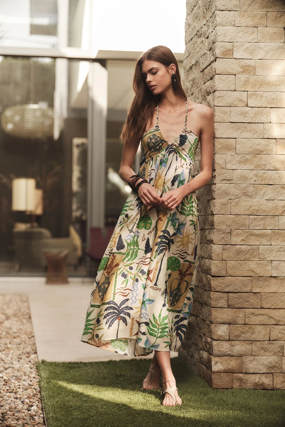 Woman in a floral dress standing against a stone wall outdoors.