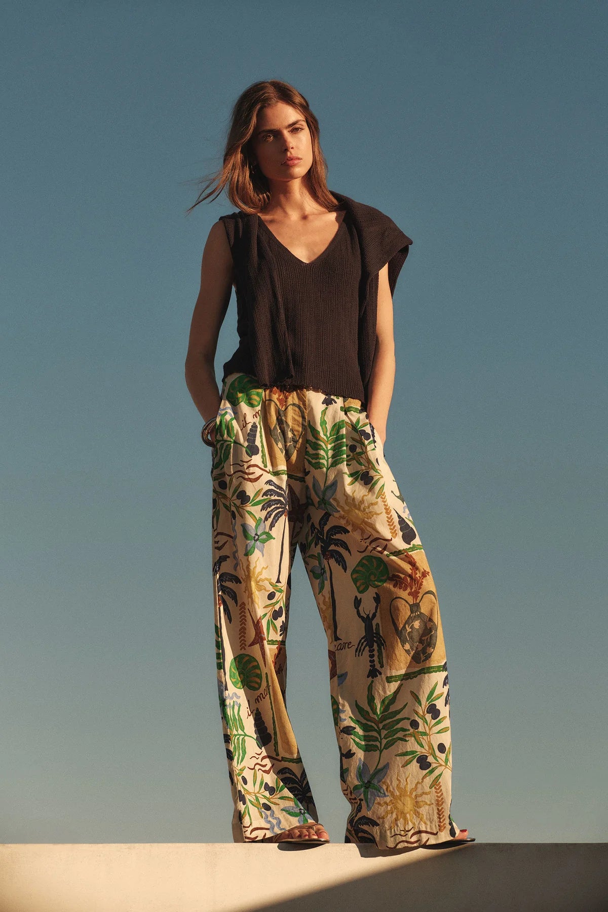 Woman wearing a black top and patterned pants against a clear blue sky.