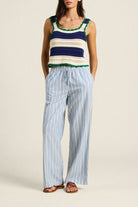 Woman wearing a colorful sleeveless top and striped pants on a beige background