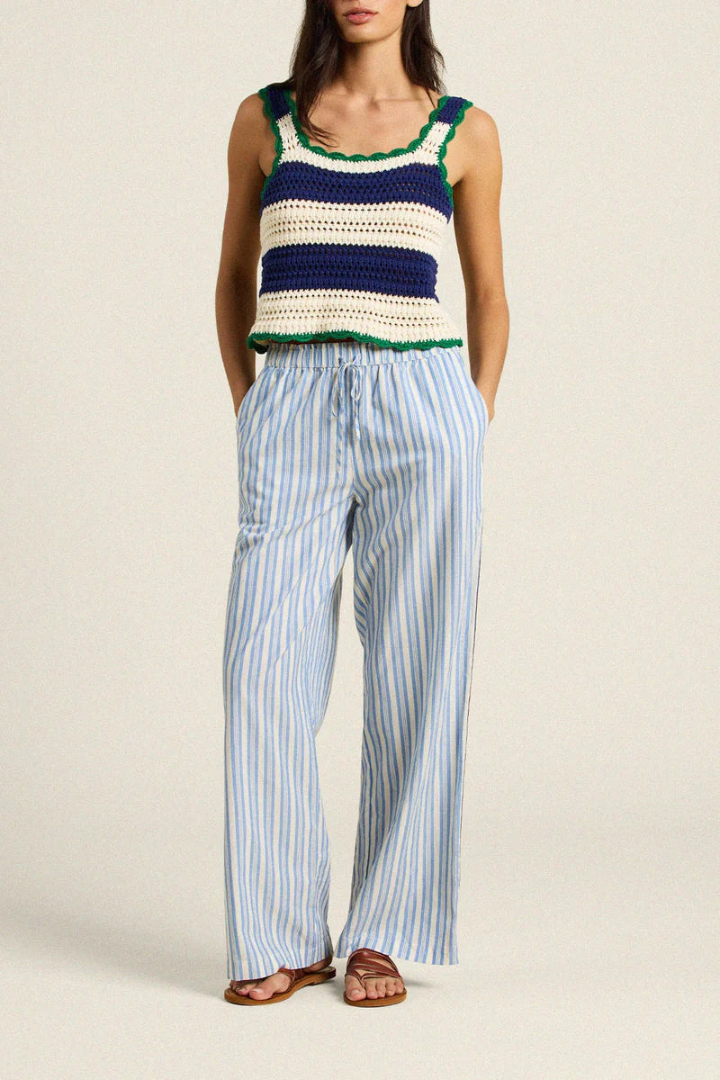 Woman wearing a colorful sleeveless top and striped pants on a beige background
