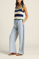 Woman wearing a striped sleeveless top and wide-leg pants on a plain background