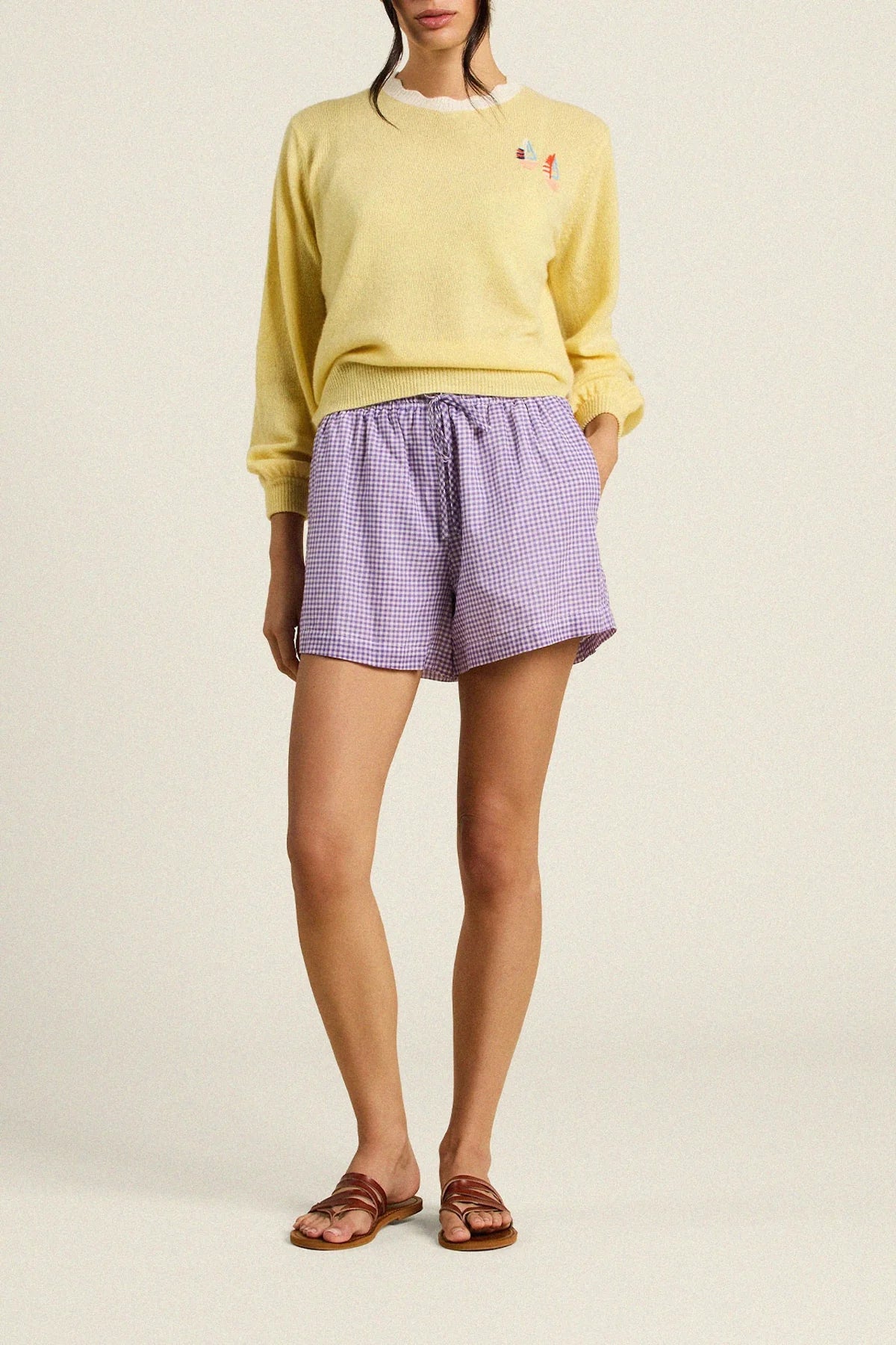 Person wearing a yellow sweater and purple checkered shorts on a beige background