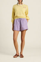 Person wearing a yellow sweater and purple checkered shorts on a beige background