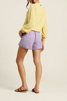 Person wearing a yellow sweater and purple checkered shorts on a beige background