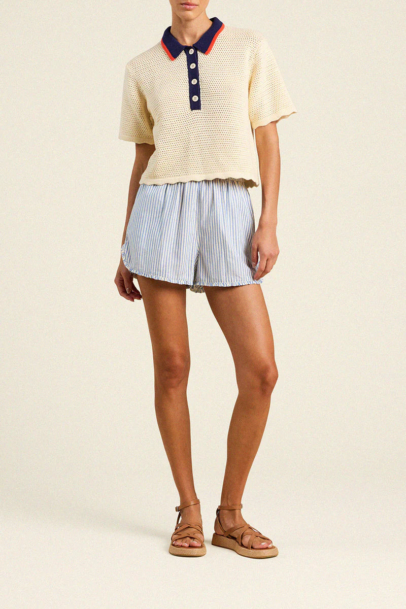 Person wearing a cream-colored short-sleeve shirt with a navy collar and blue striped shorts on a beige background