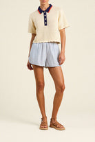 Person wearing a cream-colored short-sleeve shirt with a navy collar and blue striped shorts on a beige background