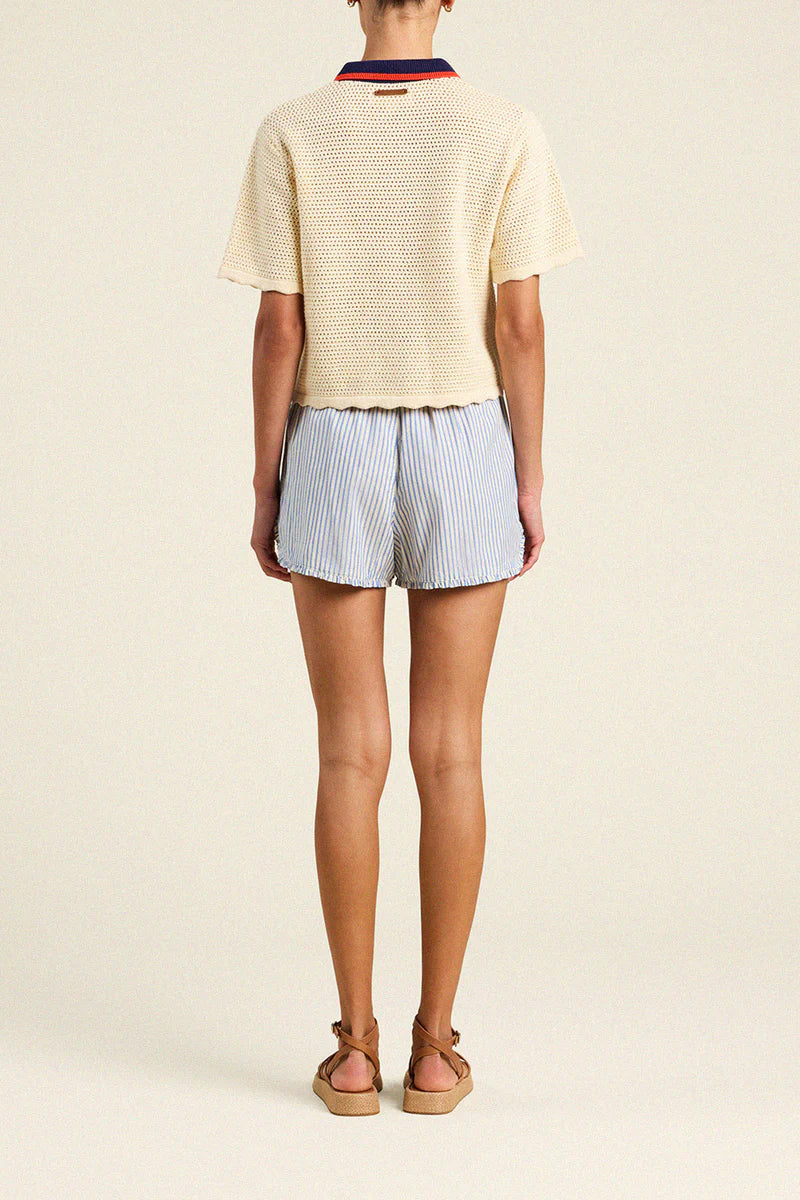 Person wearing a light-colored sweater and striped shorts on a plain background