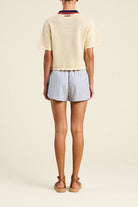 Person wearing a light-colored sweater and striped shorts on a plain background