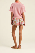 Person wearing a pink textured top and floral shorts on a beige background