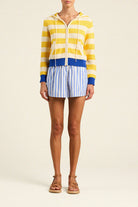 Person wearing a yellow and blue striped hoodie with white shorts on a beige background