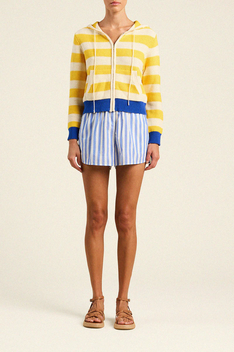 Person wearing a yellow and blue striped hoodie with white shorts on a beige background